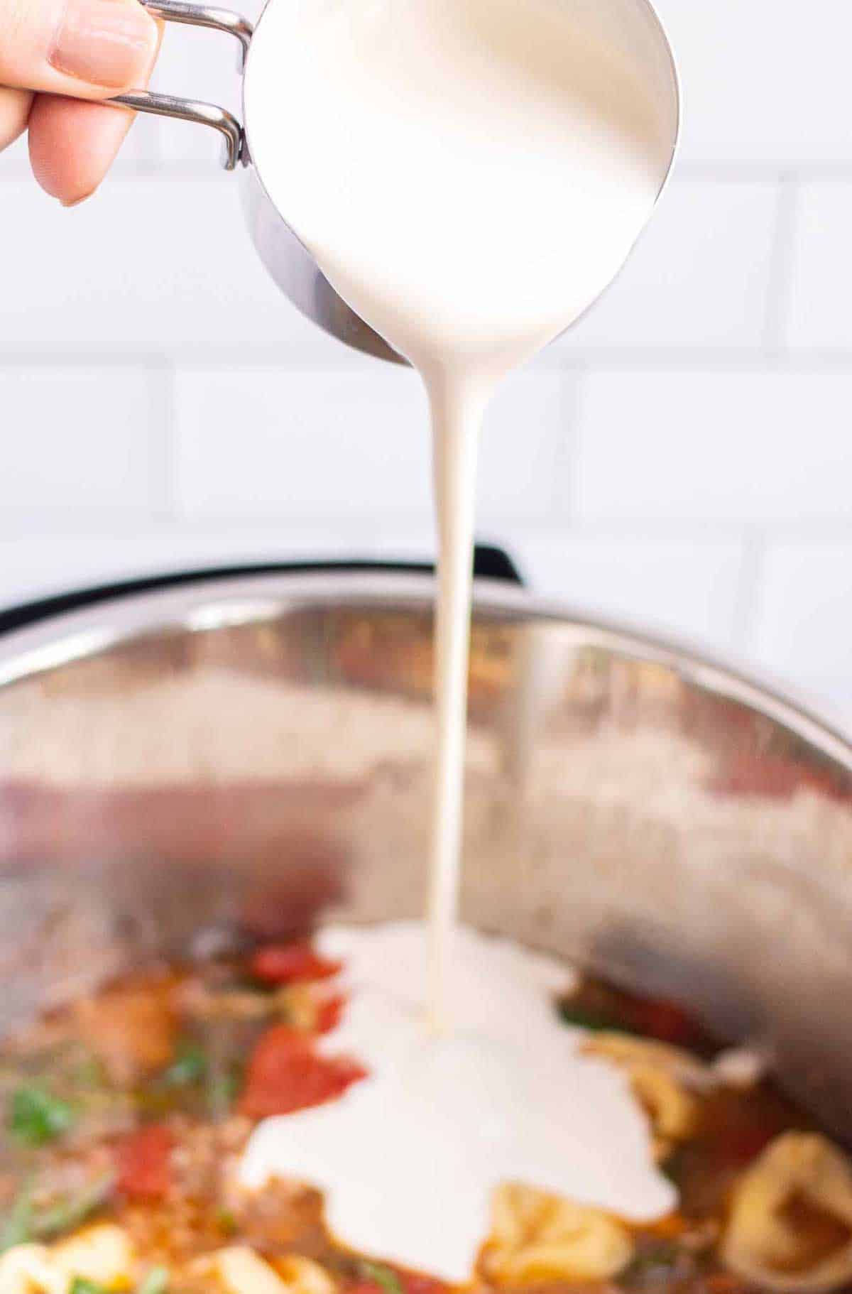 Pouring heavy whipping cream from a measuring cup into the Instant Pot.