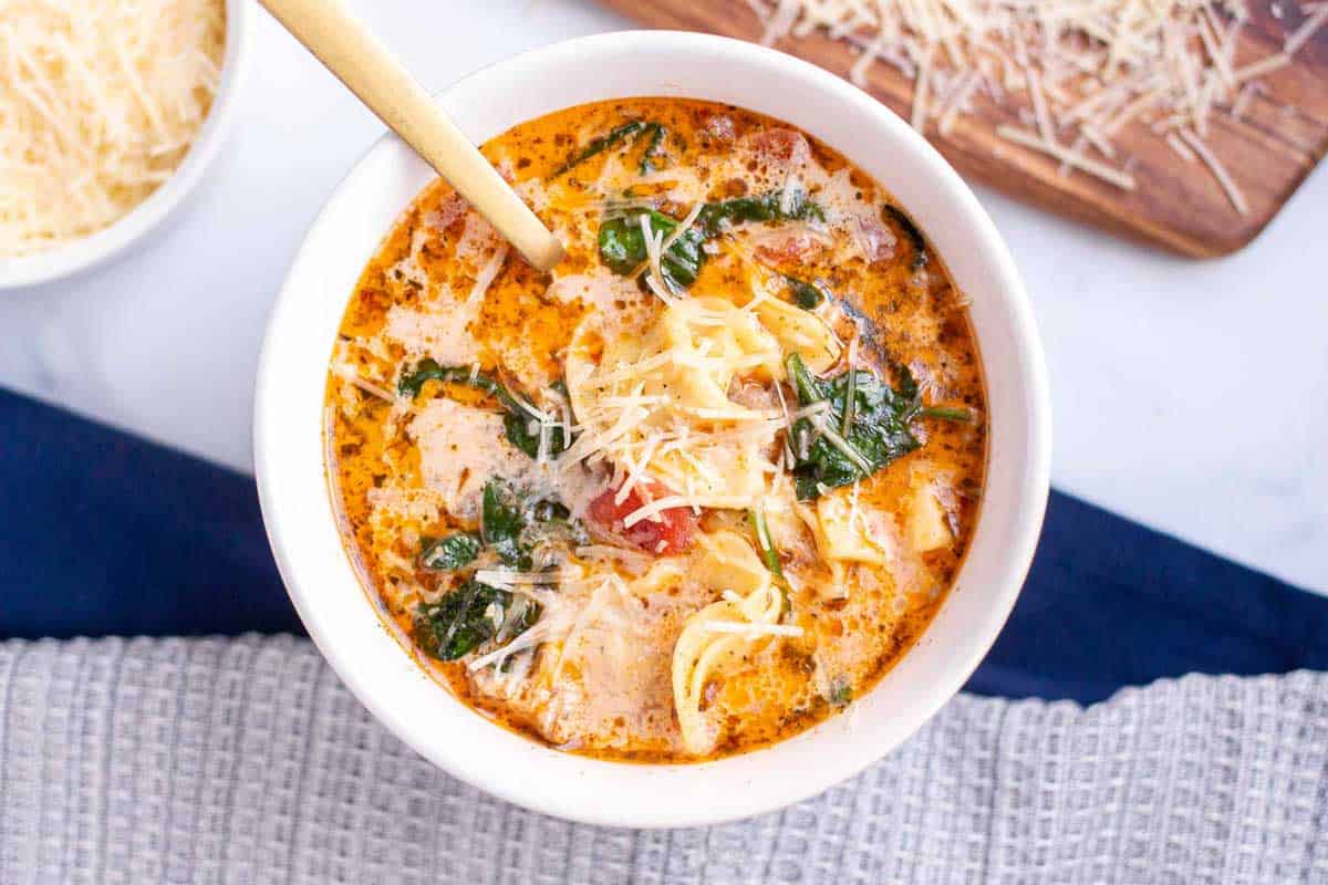 Instant Pot Tortellini Soup with tortellini, Italian sausage, and wilted baby spinach in a bowl garnished with shredded parmesan.