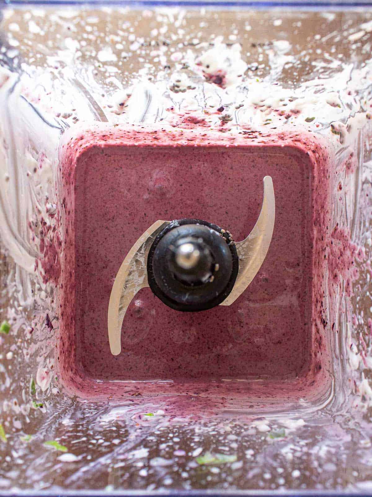 Top-down view inside a blender with blended blueberry banana spinach smoothie inside.