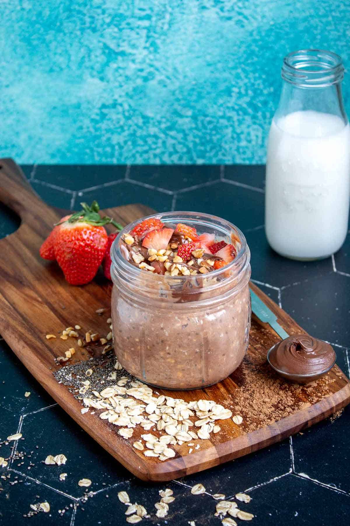 Nutella overnight oats in a mason jar topped with strawberries, Nutella, and hazelnuts.