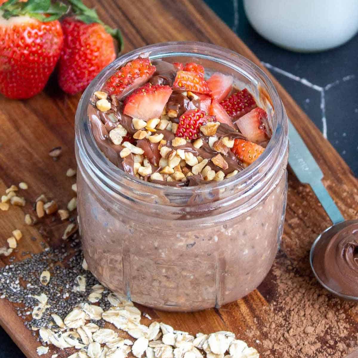 Nutella overnight oats in a mason jar topped with strawberries, Nutella, and hazelnuts.