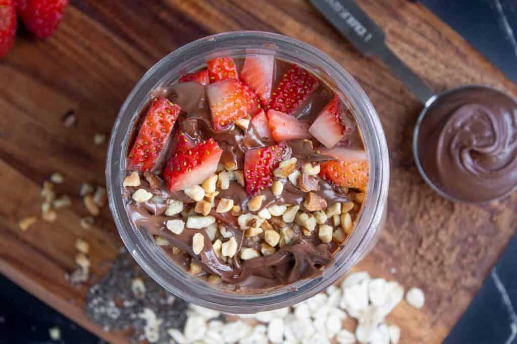 Top-down view of Nutella overnight oats in a mason jar topped with strawberries, Nutella, and hazelnuts.