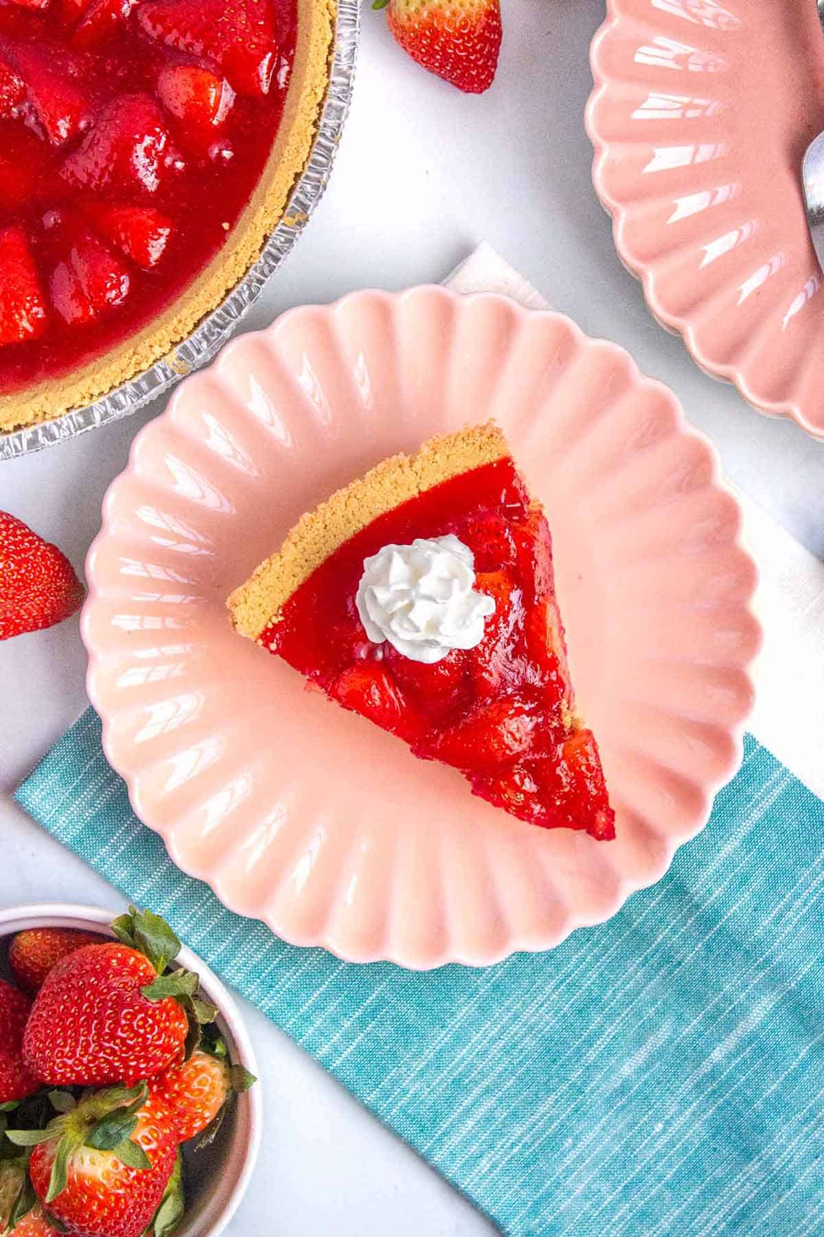 Slice of strawberry jello pie on a small plated topped with a dollop of whipped cream.