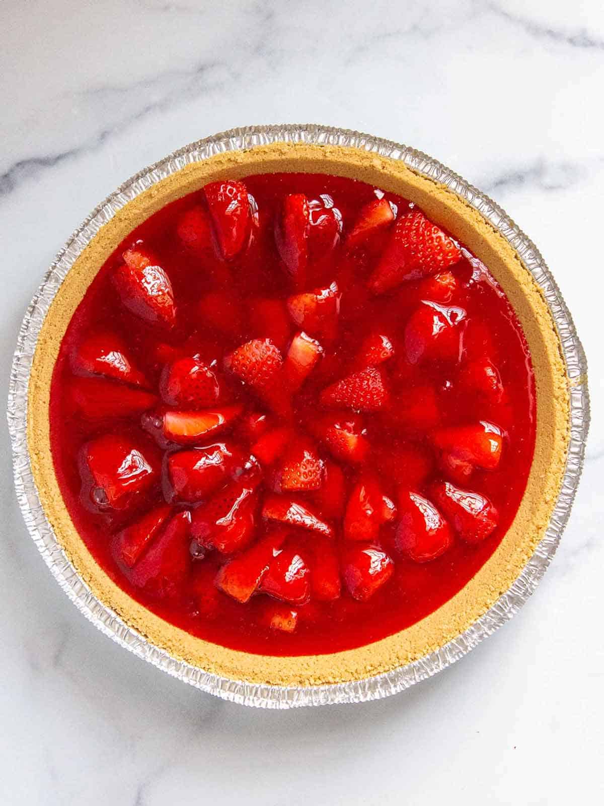 Strawberries cut side facing down in a graham cracker pie crust with jello poured evenly over top.