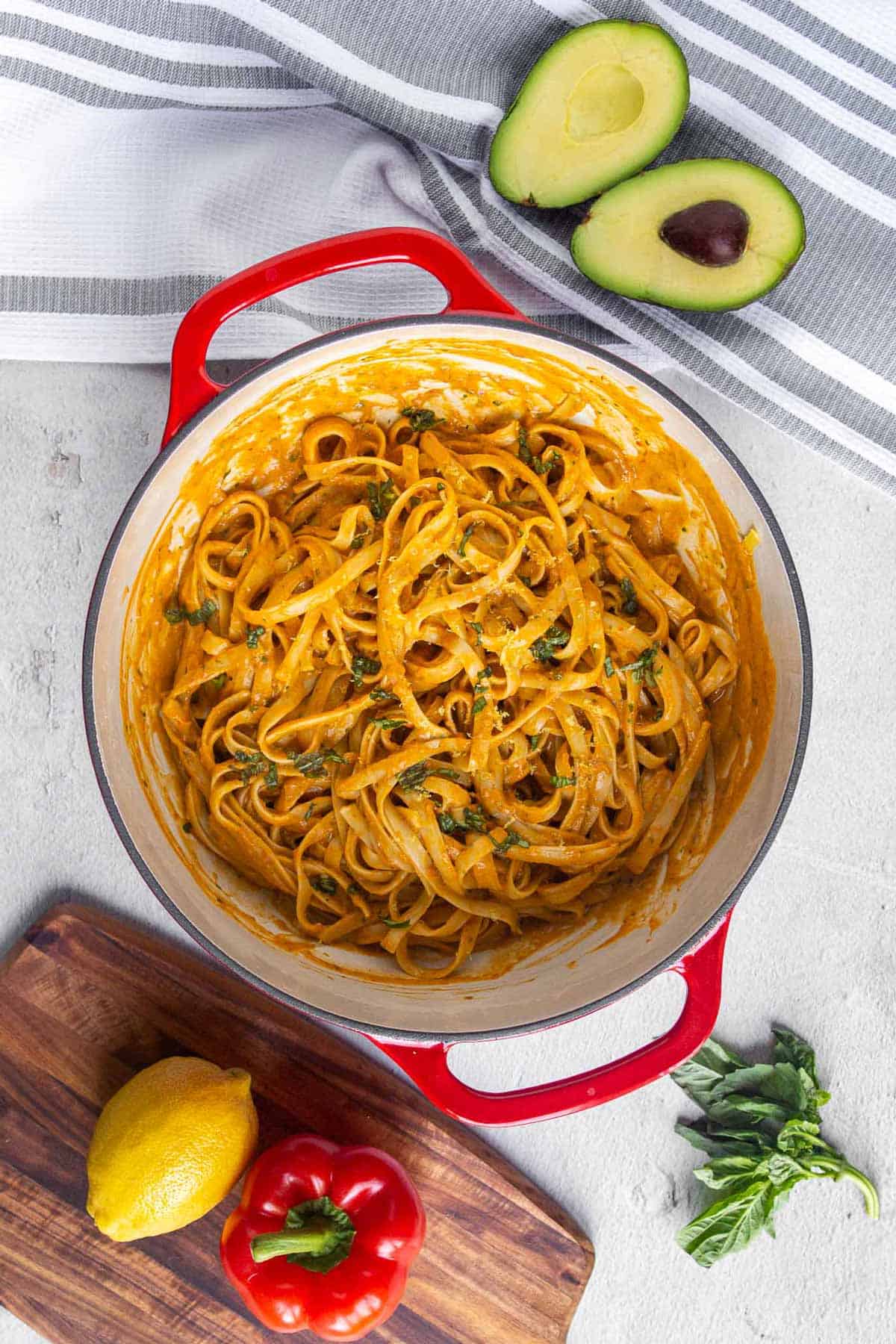 Top down view of cast iron dutch oven filled with fettuccine coated in creamy roasted red pepper sauce and garnished with fresh basil. The sauce is thick and creamy.