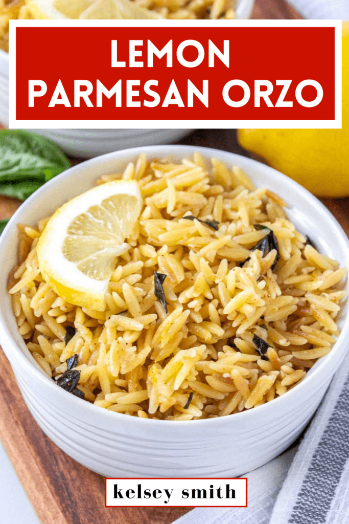 Ramekin filled with lemon parmesan orzo topped with a half lemon slice. There is fresh basil and lemon in the background. Text at the top says Lemon Parmesan Orzo.