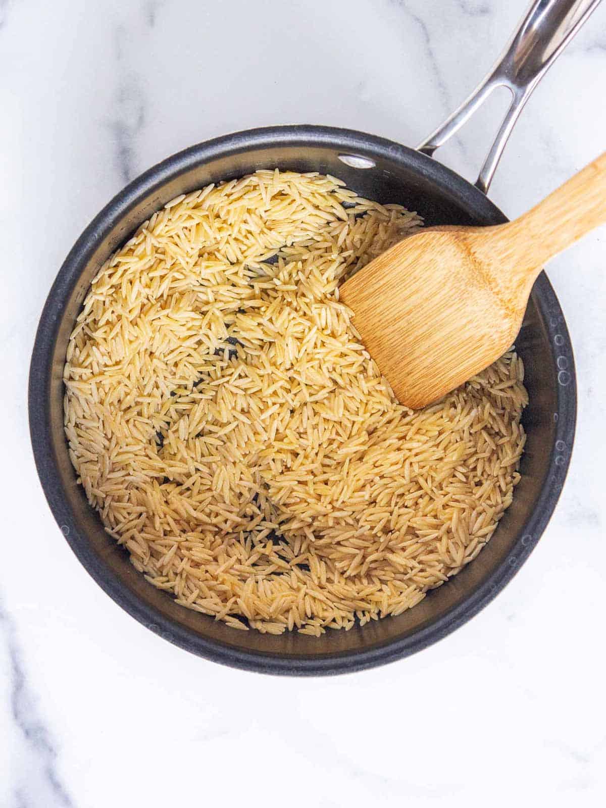 Uncooked orzo coated in butter in a medium saucepan.