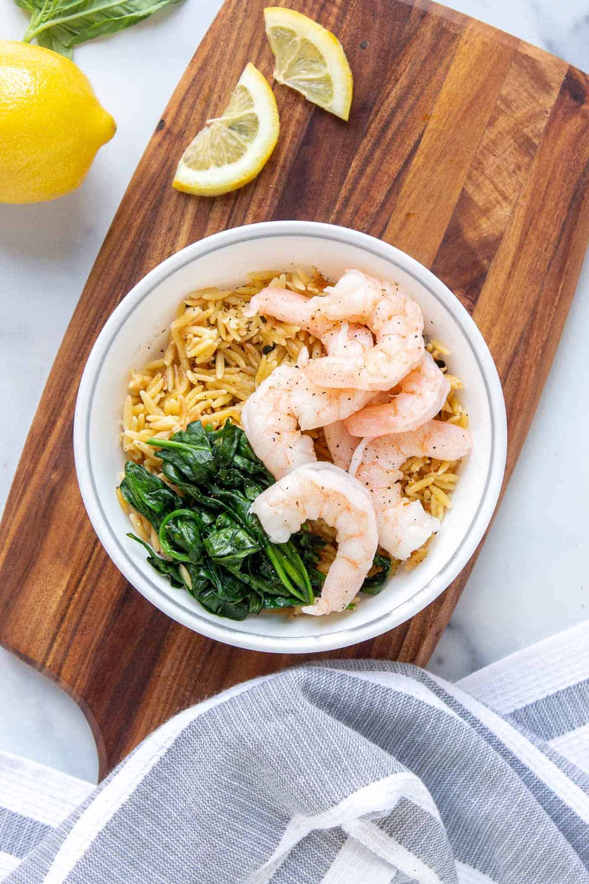 Small bowl of lemon parmesan orzo topped with shrimp and wilted baby spinach.