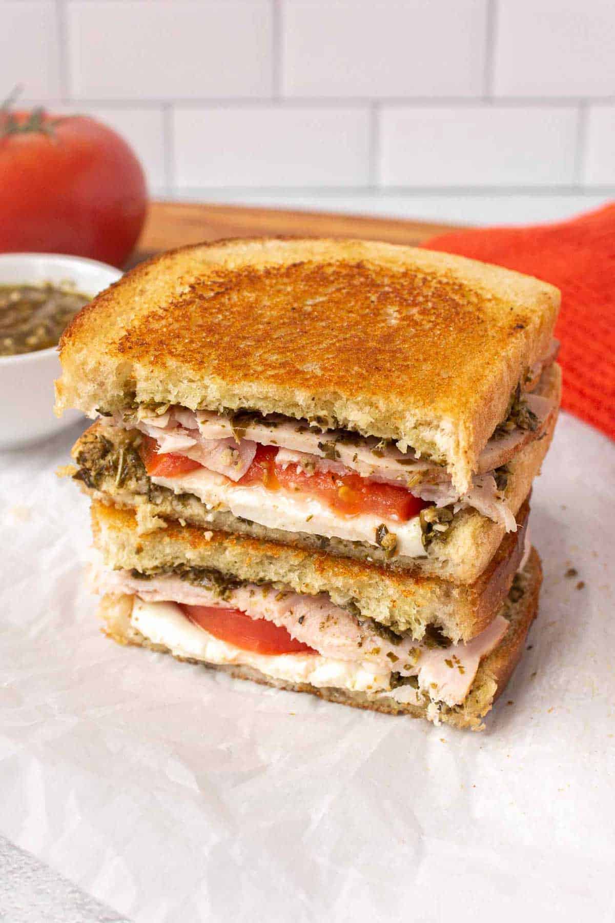 Pesto turkey sandwich cross section with pesto, fresh mozzarella slices, tomato, and thick turkey slices. The sandwich has been grilled and is golden on top.