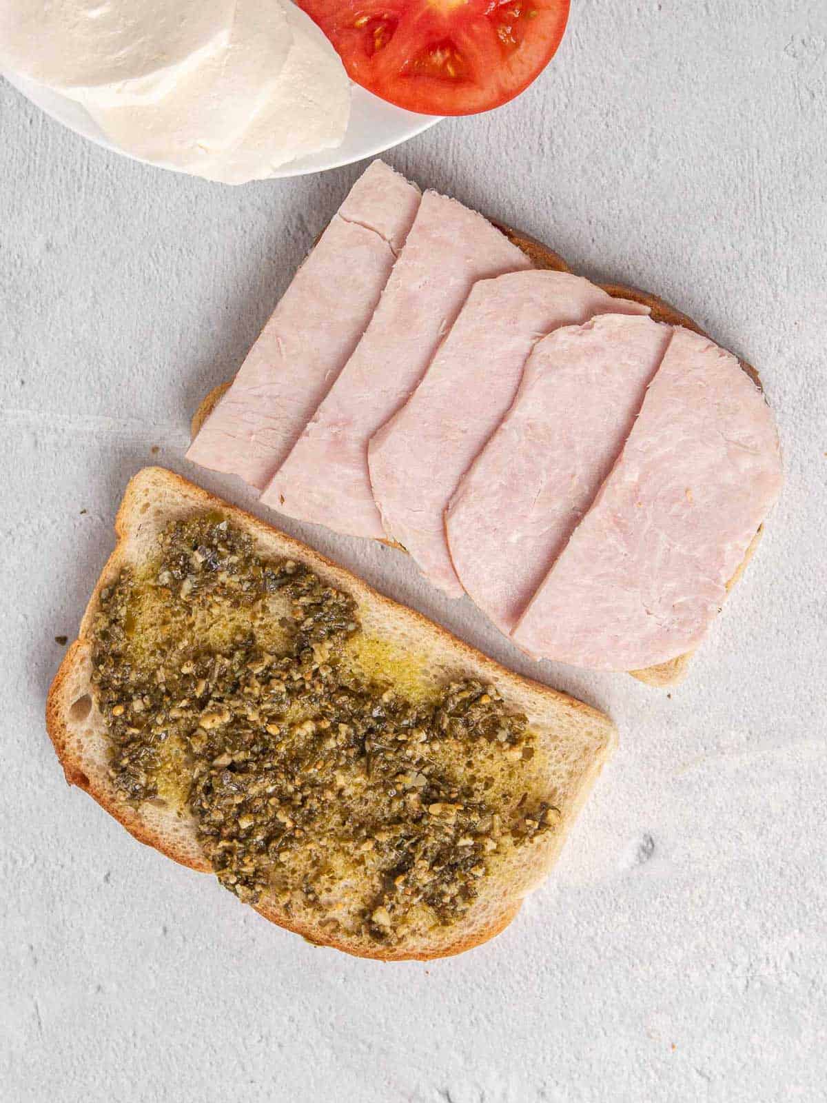Two pieces of sourdough bread with pesto layered across the top. One one slice of bread, thick slices of turkey are layered on top.