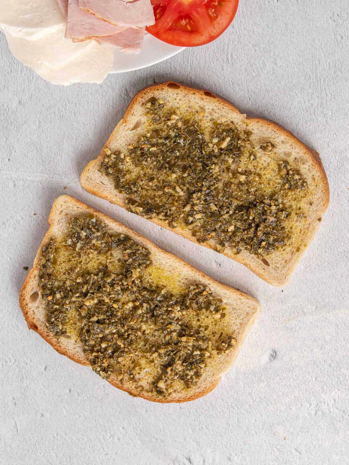 Two pieces of sourdough bread with pesto layered across the top.