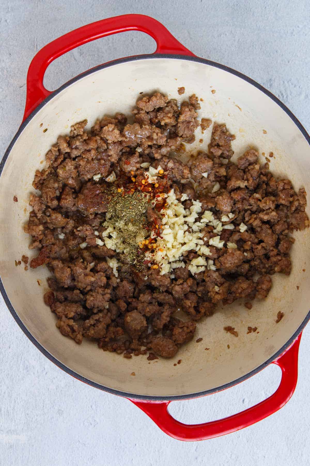Garlic, Italian seasoning, and red pepper flakes added to cooked Italian sausage in a large pot