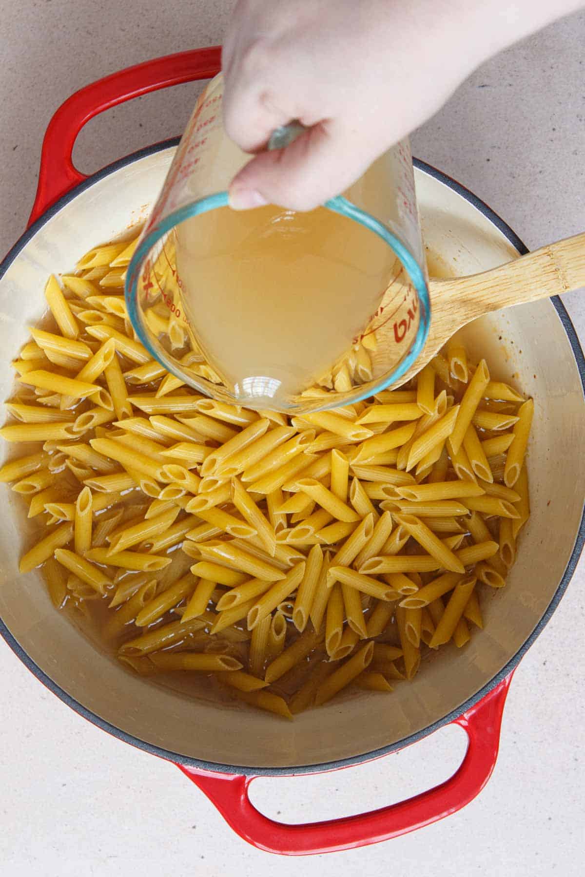 Pouring broth into the pot over the penne