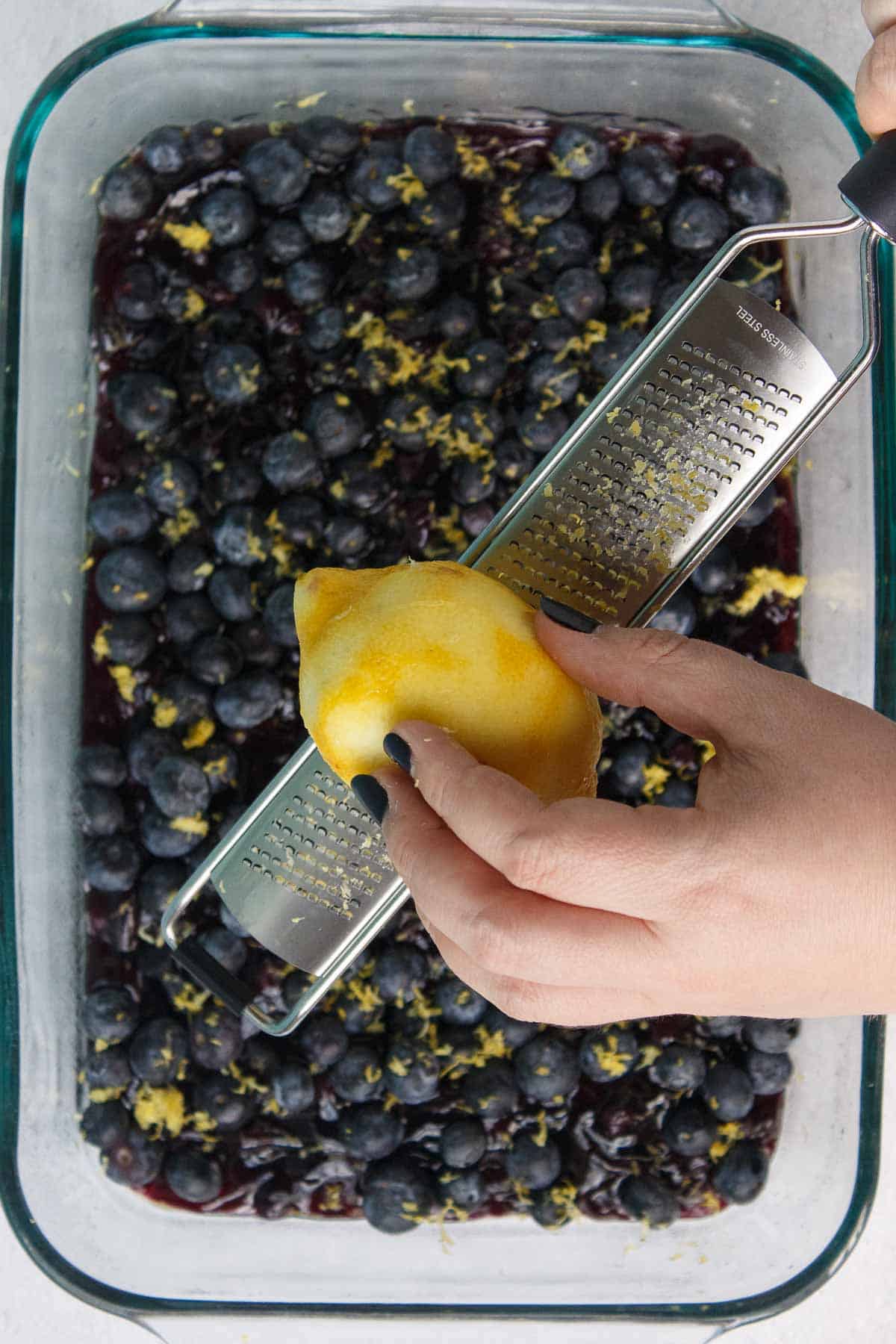 Fresh lemon being zested over blueberries