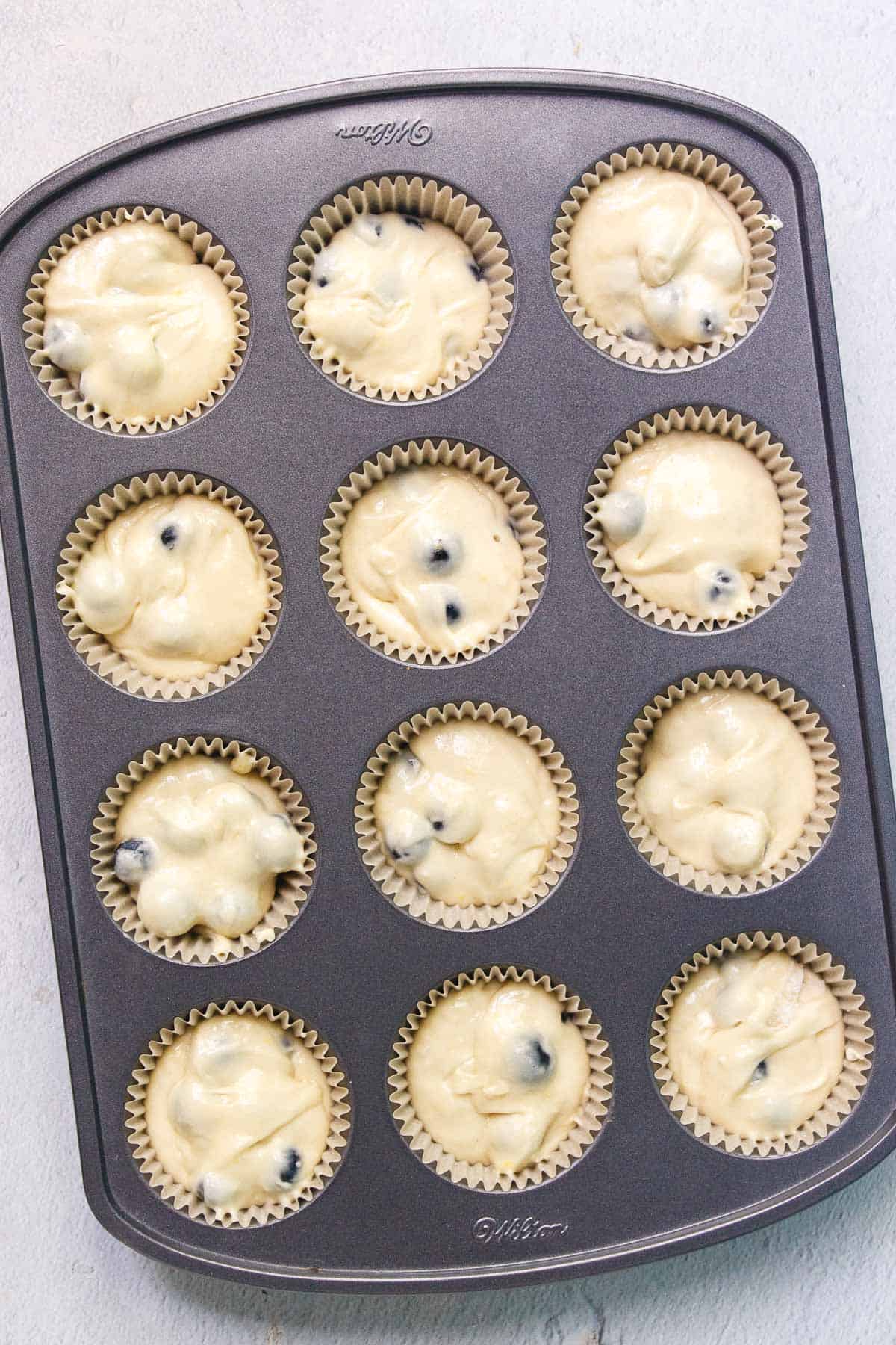 Cake mix blueberry muffin batter in lined muffin tins. Each liner is filled with a half inch of space at the top.