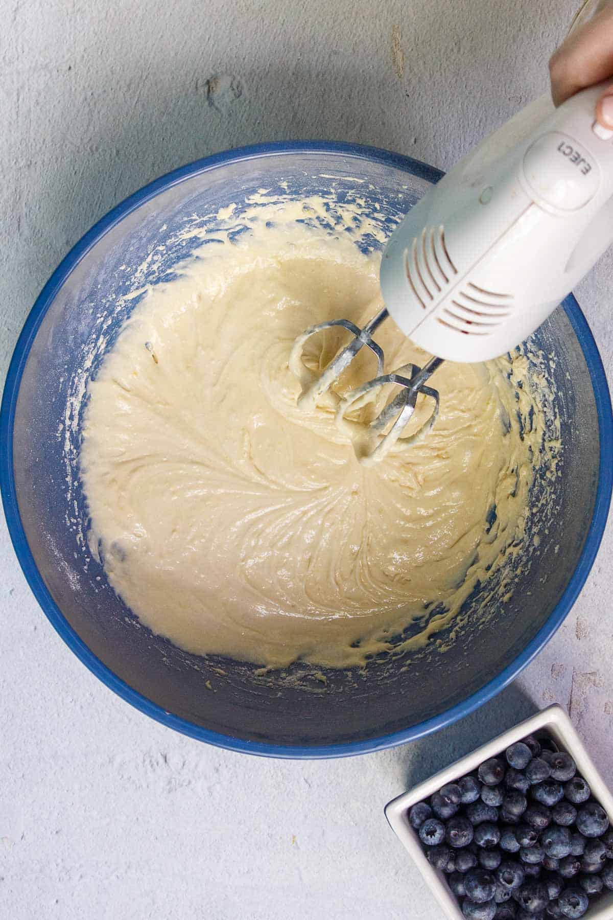 Beating cake mix blueberry muffin batter with a hand mixer in a large mixing bowl
