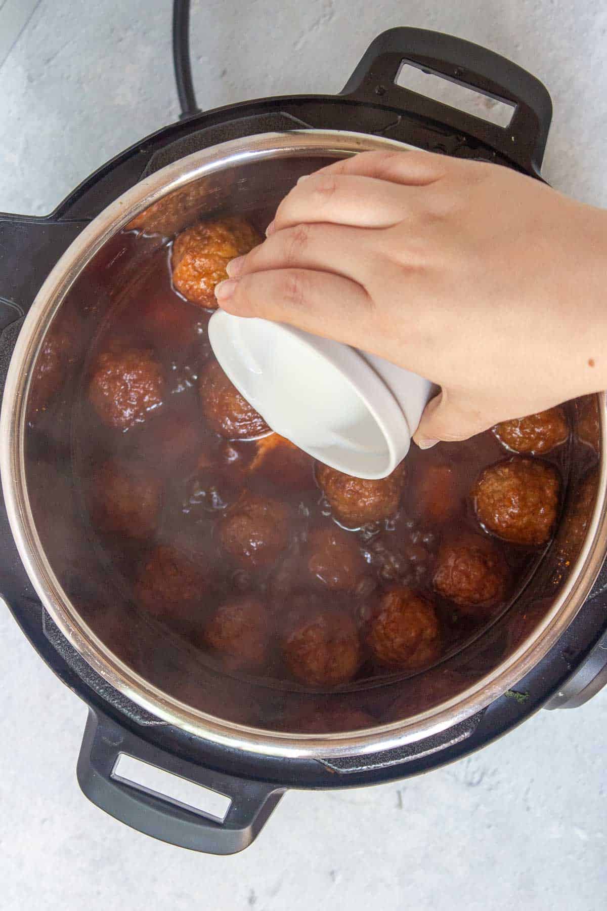 Pouring a cornstarch slurry over the meatballs in the Instant Pot