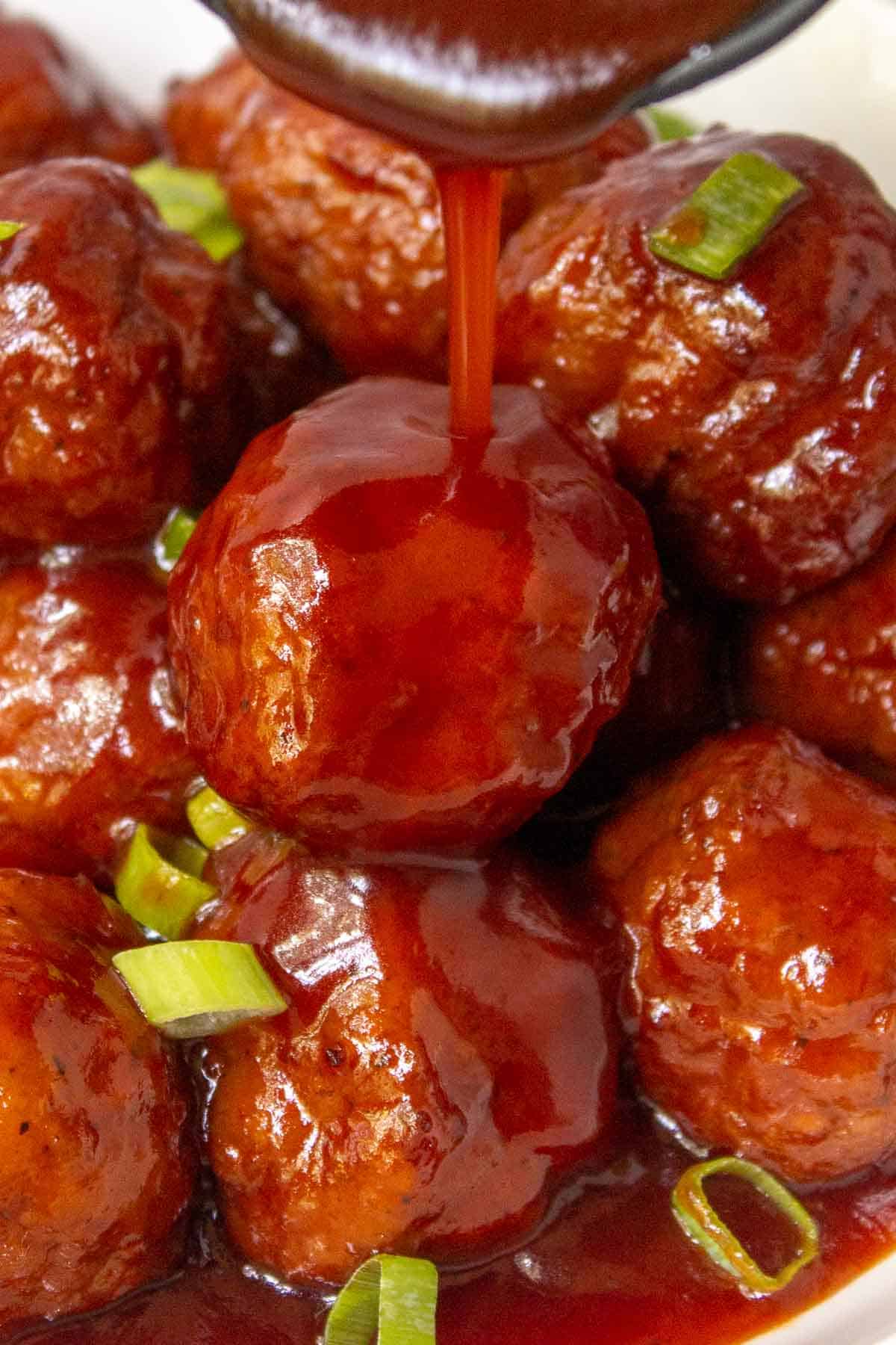 Grape jelly sauce being poured over a pile of Instant Pot Grape Jelly Meatballs