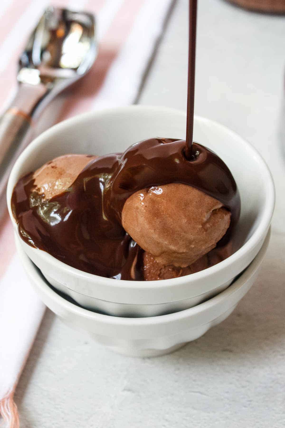 Pouring chocolate syrup over scoops of Ninja Creami Chocolate Protein Ice Cream in a small bowl