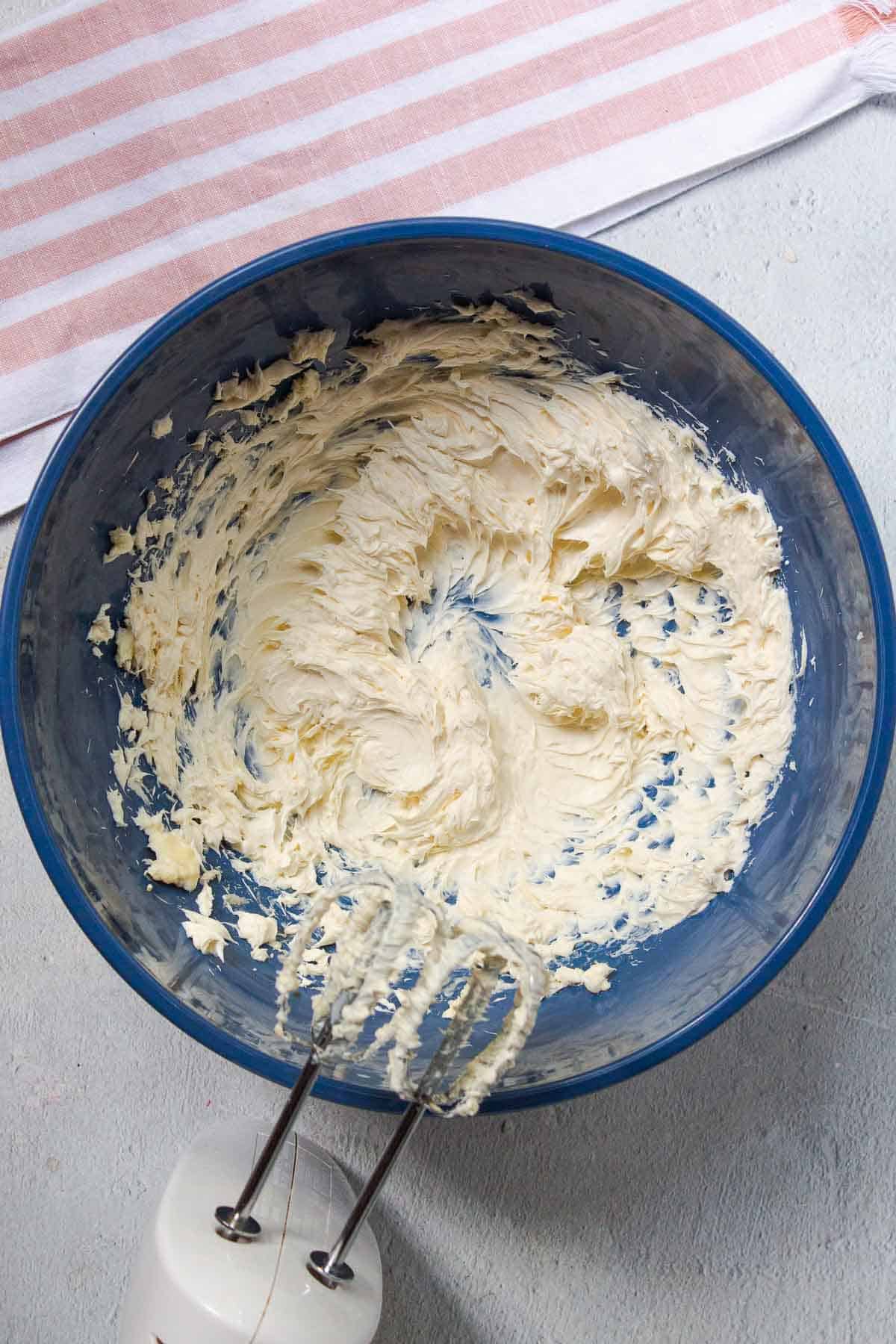 The softened cream cheese, softened butter, and vanilla are beaten together with a hand mixer in a large mixing bowl until light and fluffy