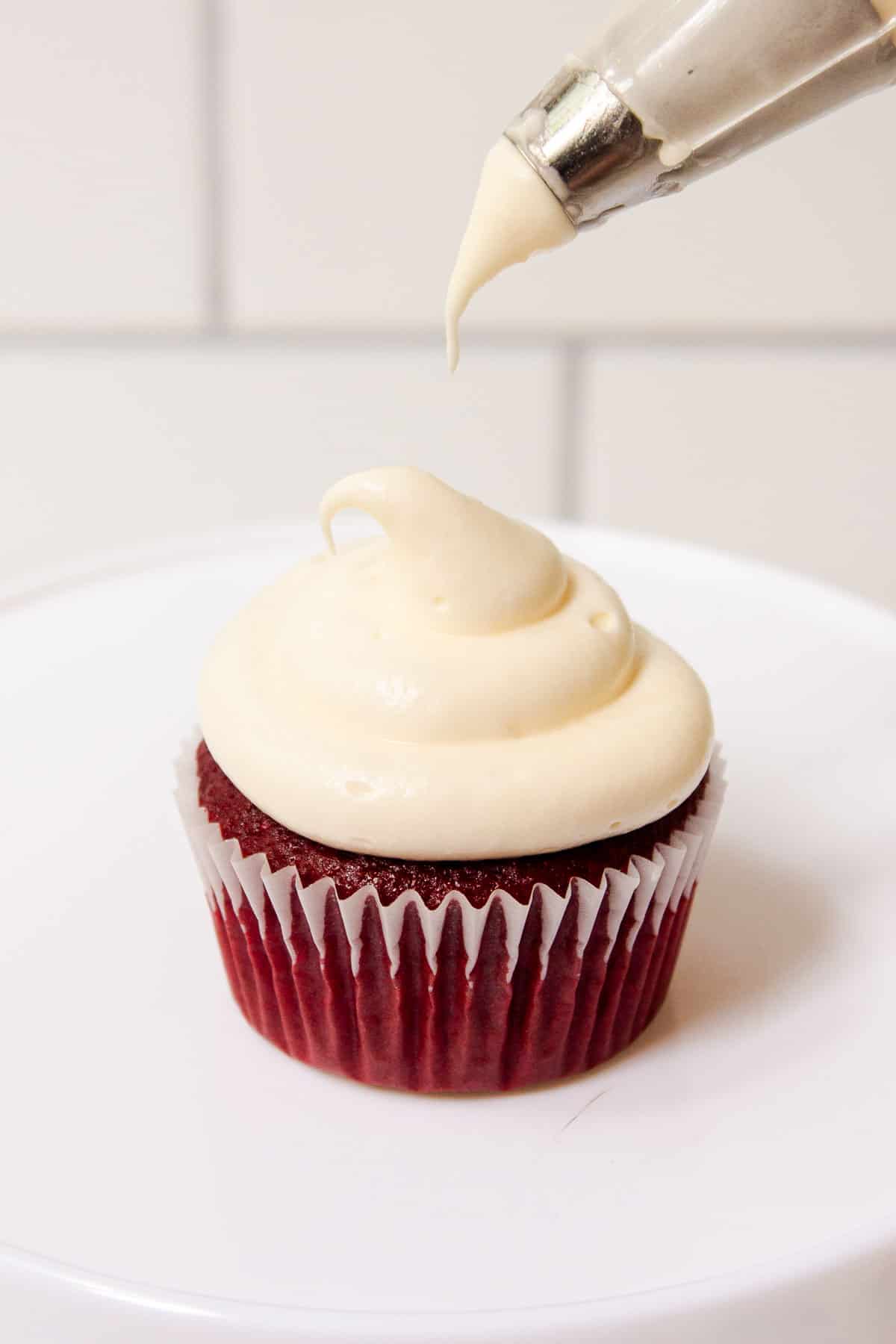 Cool Whip Cream Cheese Frosting being piped onto a red velvet cupcake with a 1A decorating tip