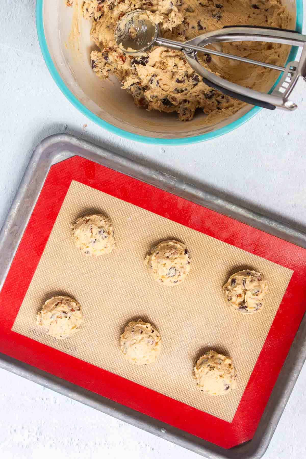The chocolate chip pecan cookie dough is scooped onto a lined baking sheet into uniform balls that are evenly spaced apart