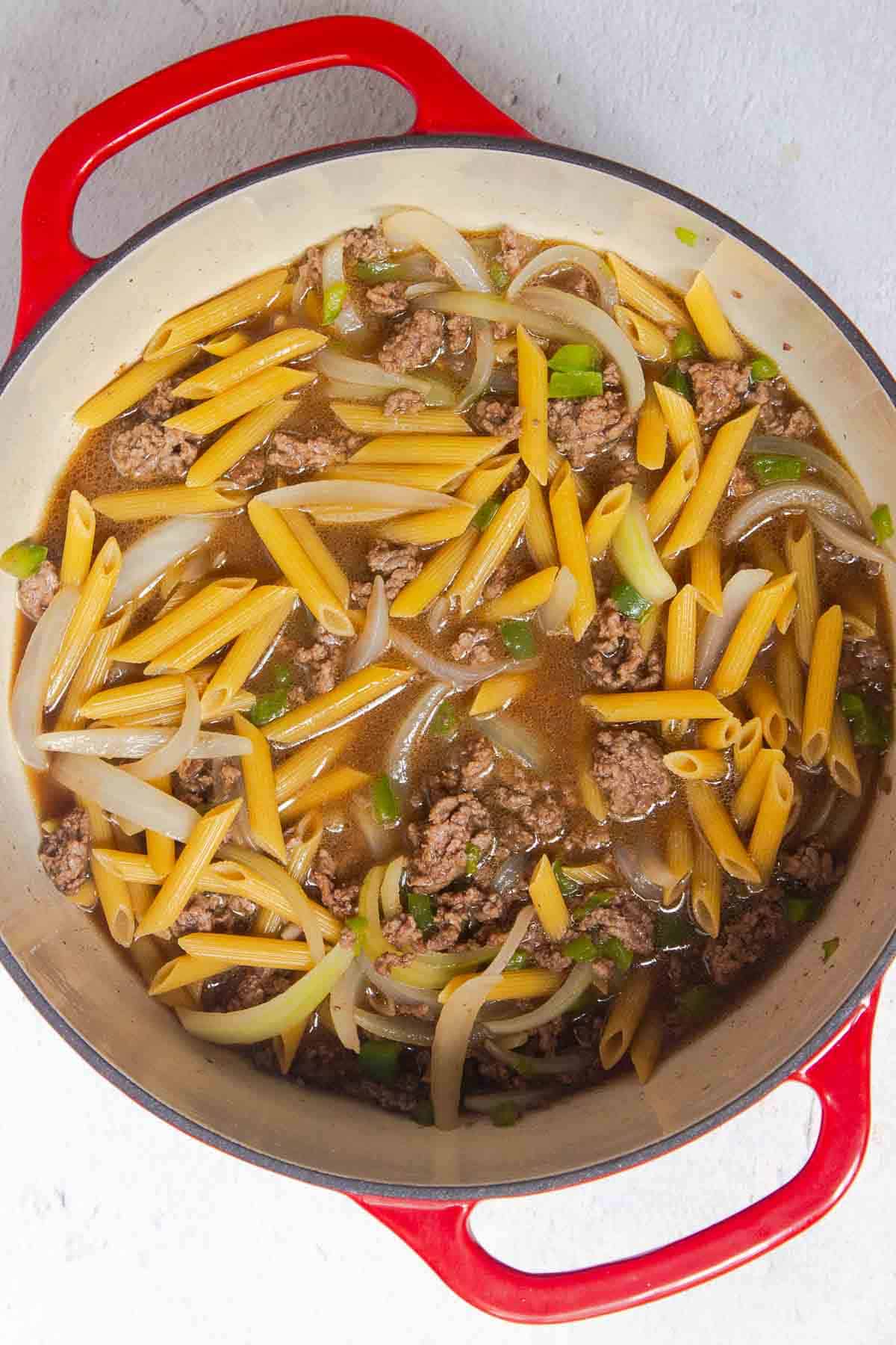 Uncooked pasta and beef broth are added to the meat mixture in the large pot