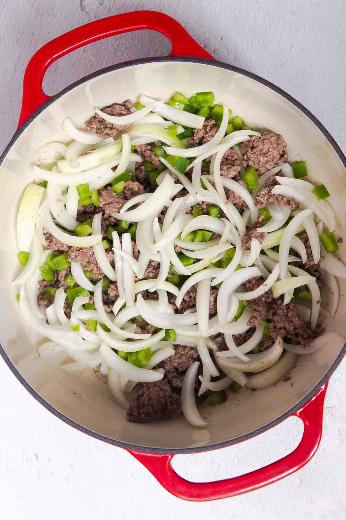 Sliced onions and diced green bell peppers are added to the browned beef