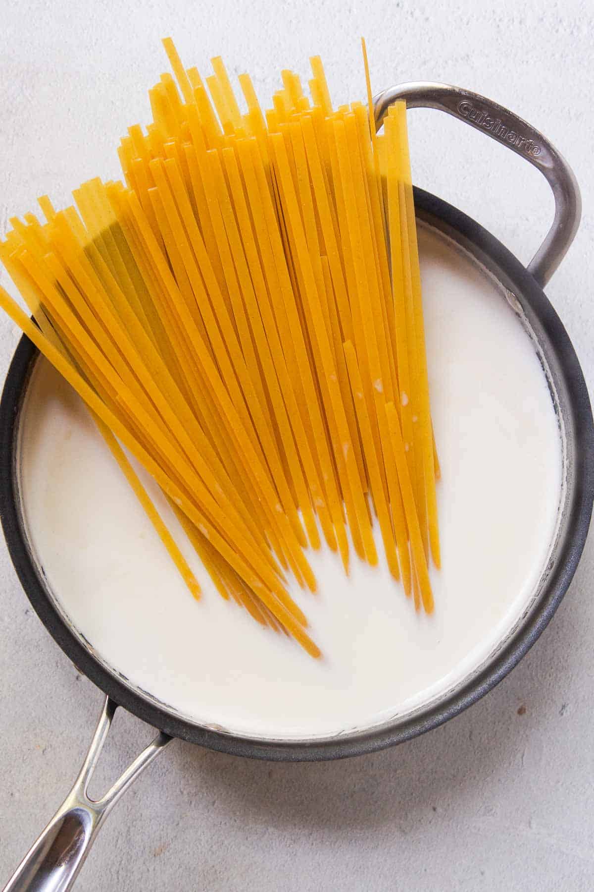 Uncooked fettuccine pasta is added to the boiling milk and broth mixture
