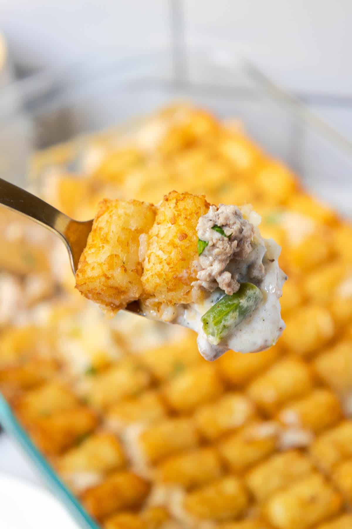 A bite of green bean tater tot casserole showing cut green beans, ground beef, and crispy tater tots.