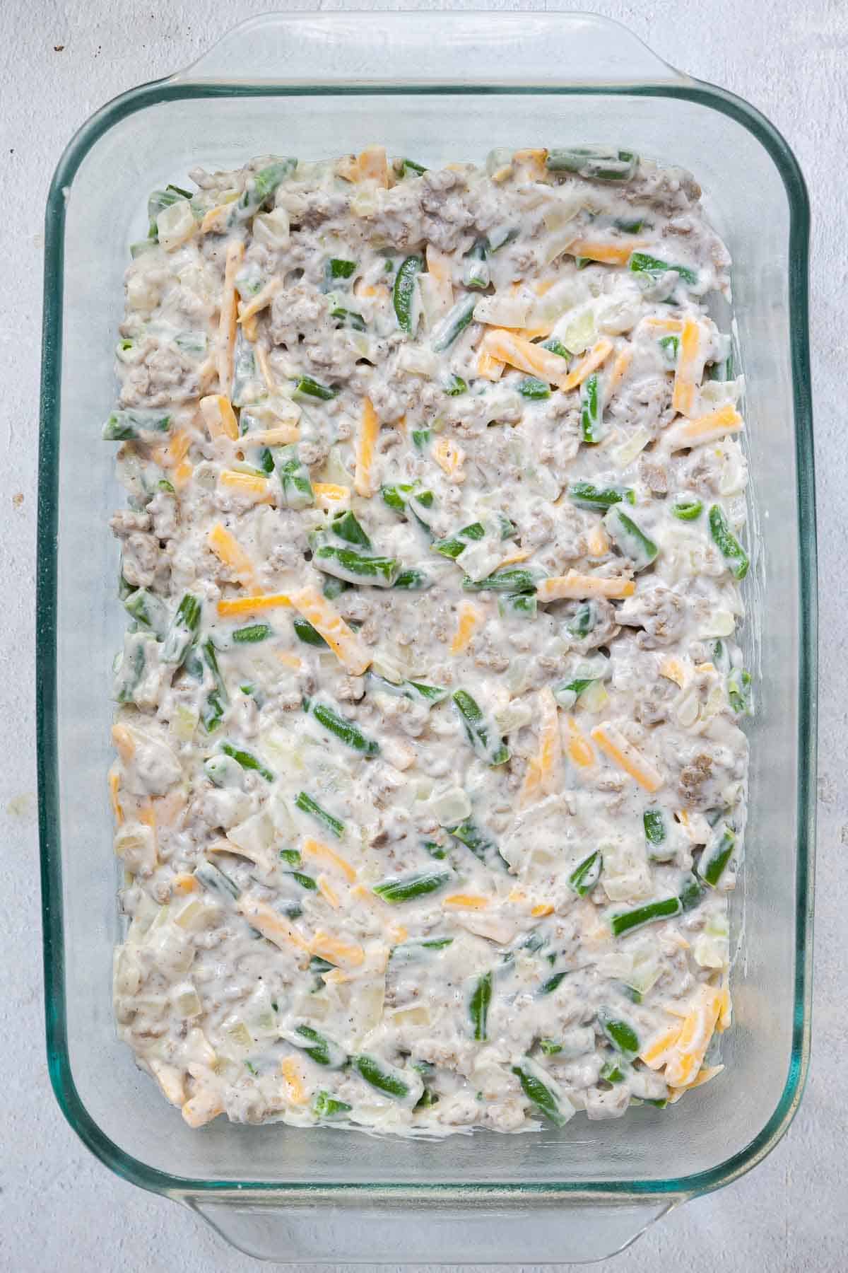 The green bean and meat mixture is spread evenly in the bottom of a 9 by 13 inch casserole dish.