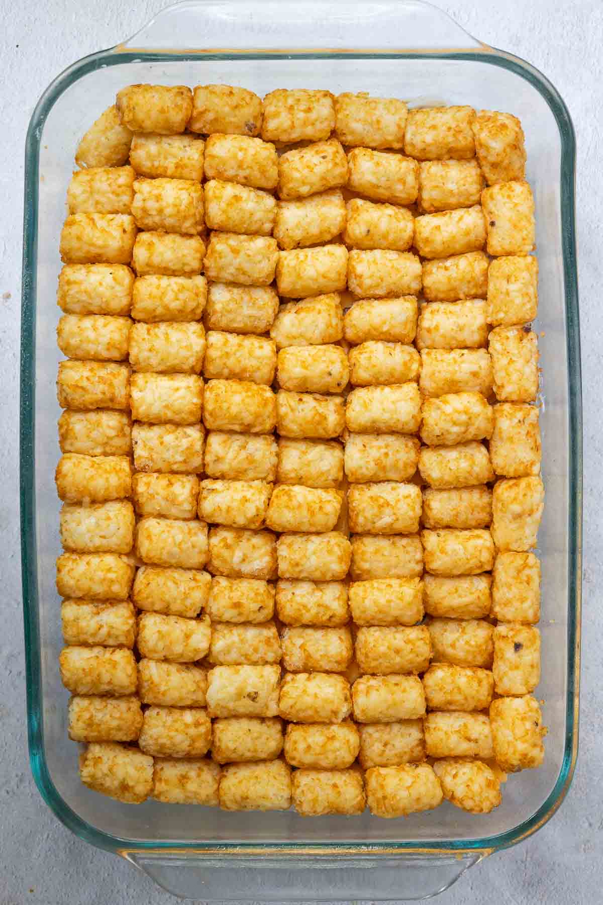 Tater tots are placed on their side in a single layer over the entire casserole dish.