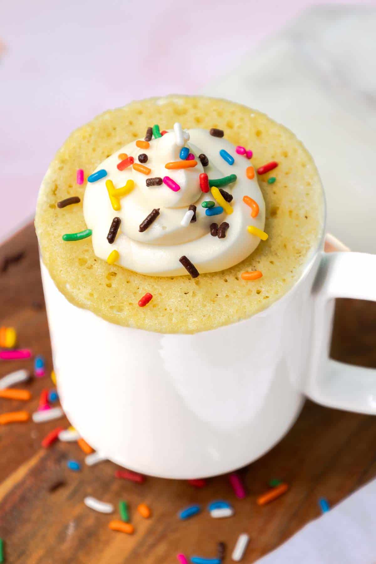 Yellow mug cake topped with buttercream frosting and sprinkles