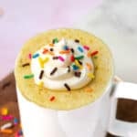 Yellow mug cake topped with buttercream frosting and sprinkles.