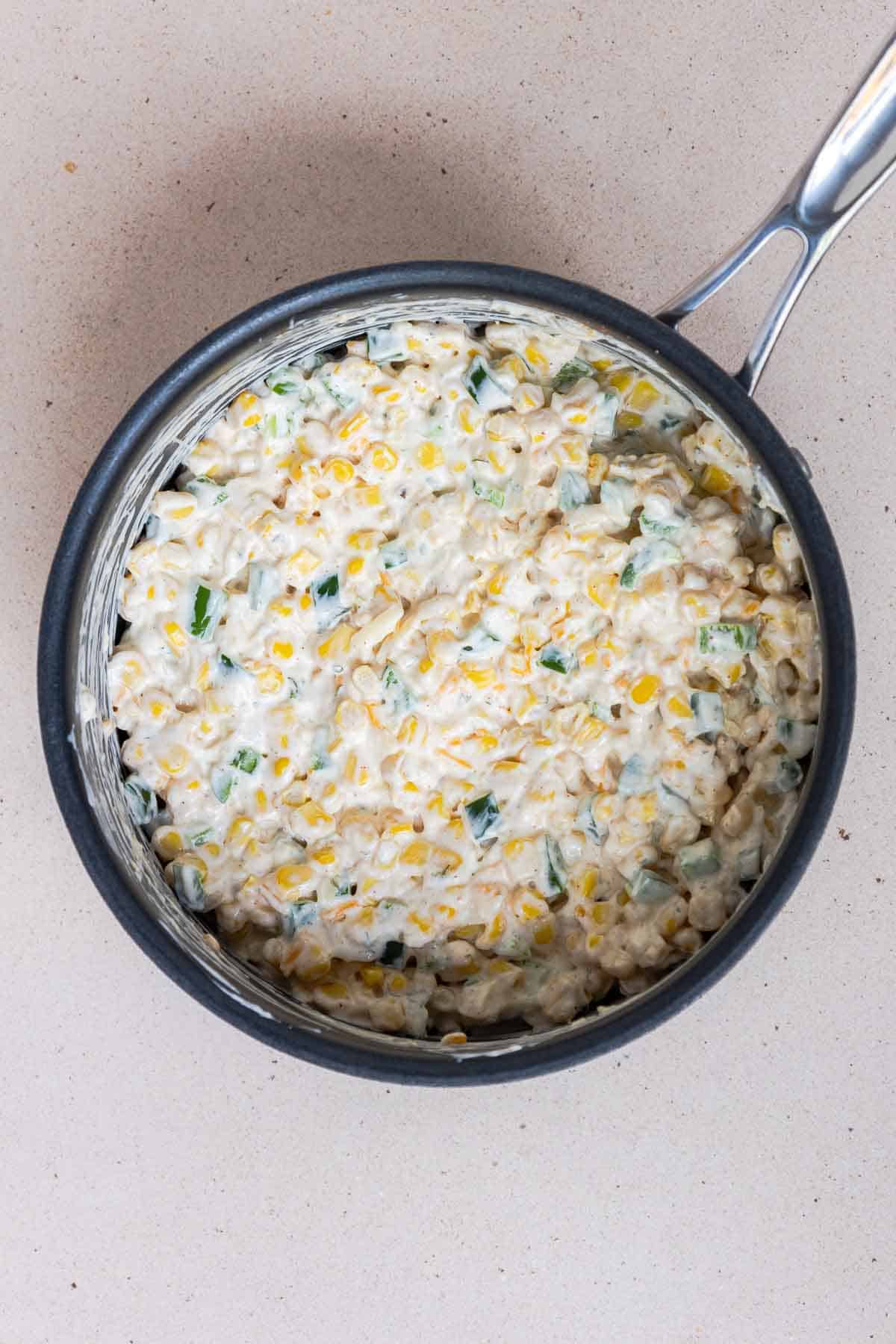 The corn casserole ingredients are coated evenly in the cream cheese mixture in the saucepan.