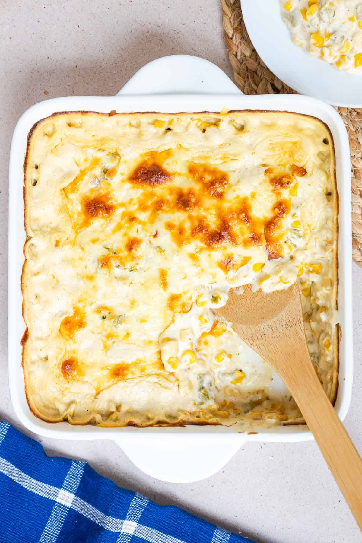 A serving of Green Chile Corn Casserole is scooped out of the baking dish to show the creamy consistency.
