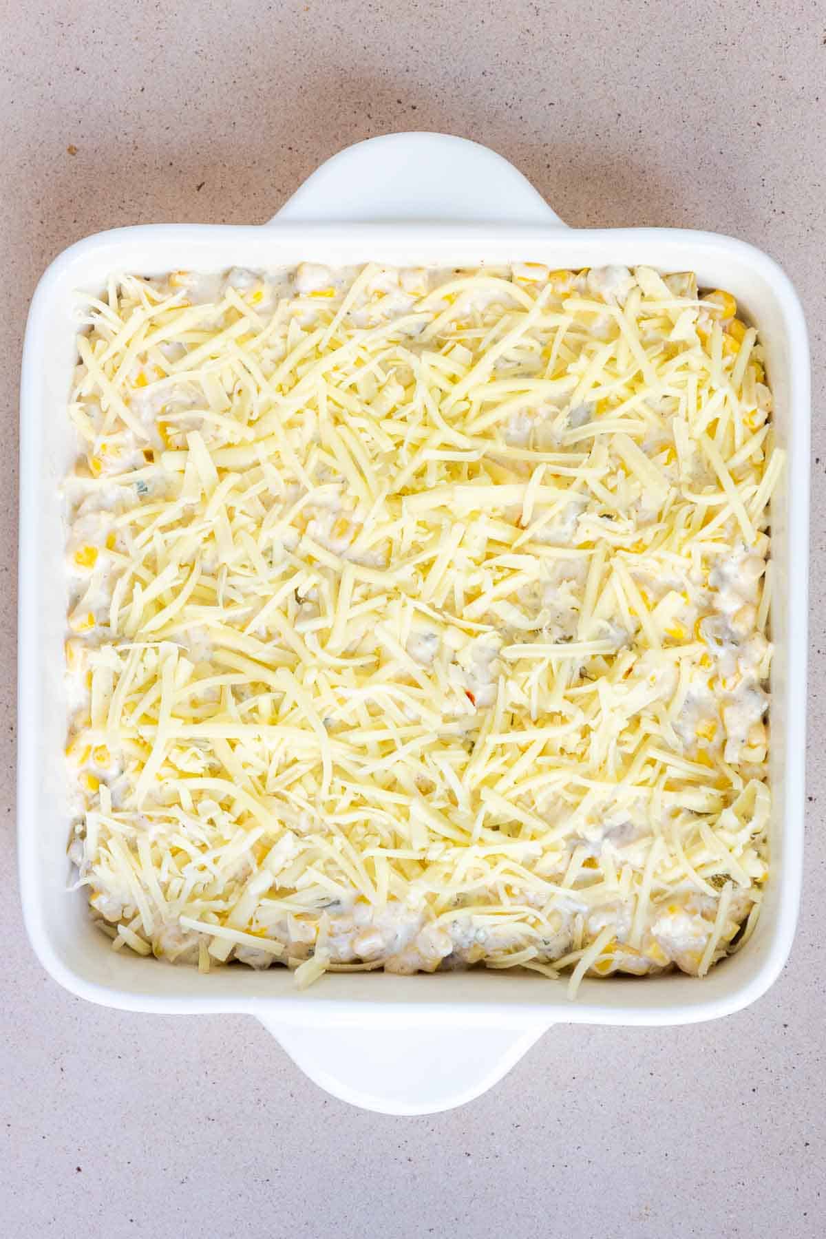 The corn casserole is topped with an even layer of shredded cheeses.