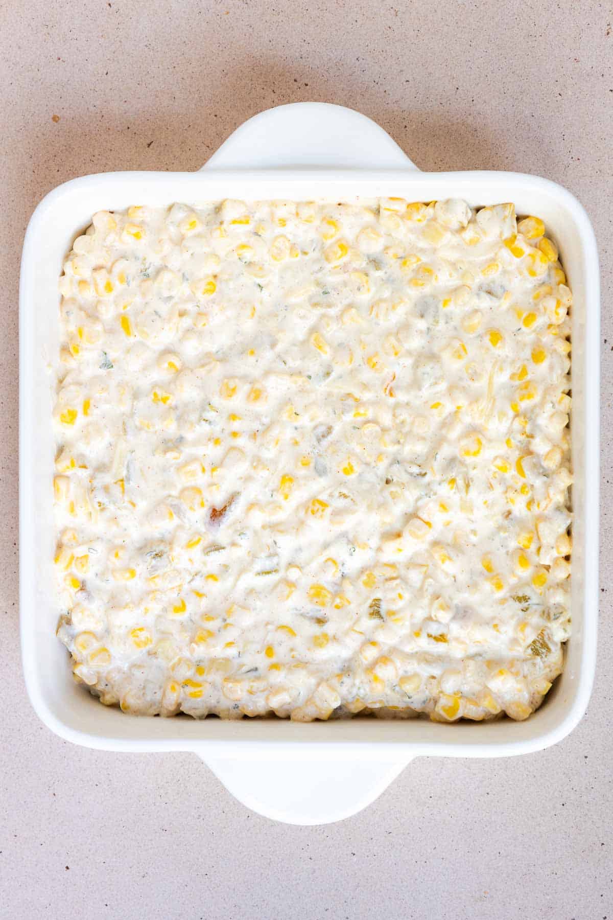 The corn casserole mixture is transferred to an 8 by 8 inch baking dish.