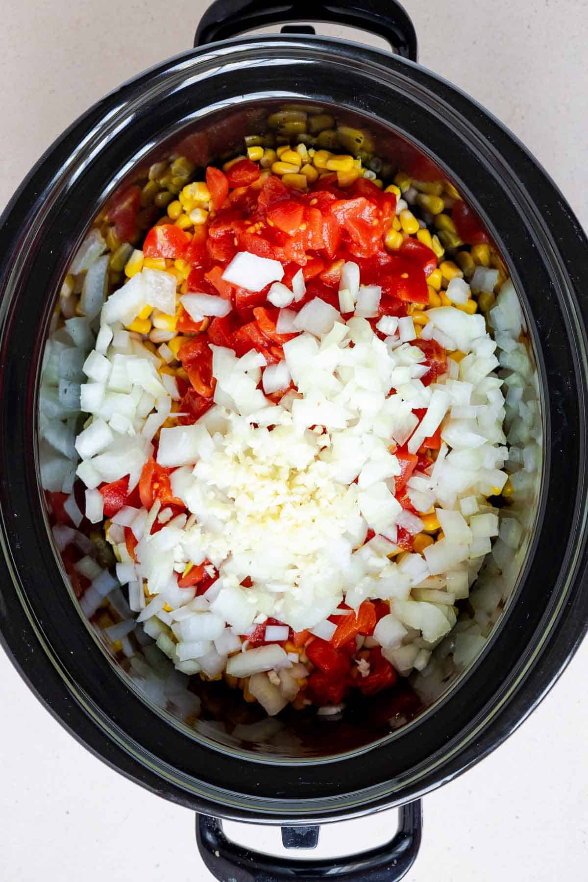 The beans, corn, tomatoes, onion, and garlic are added on top of the chicken.