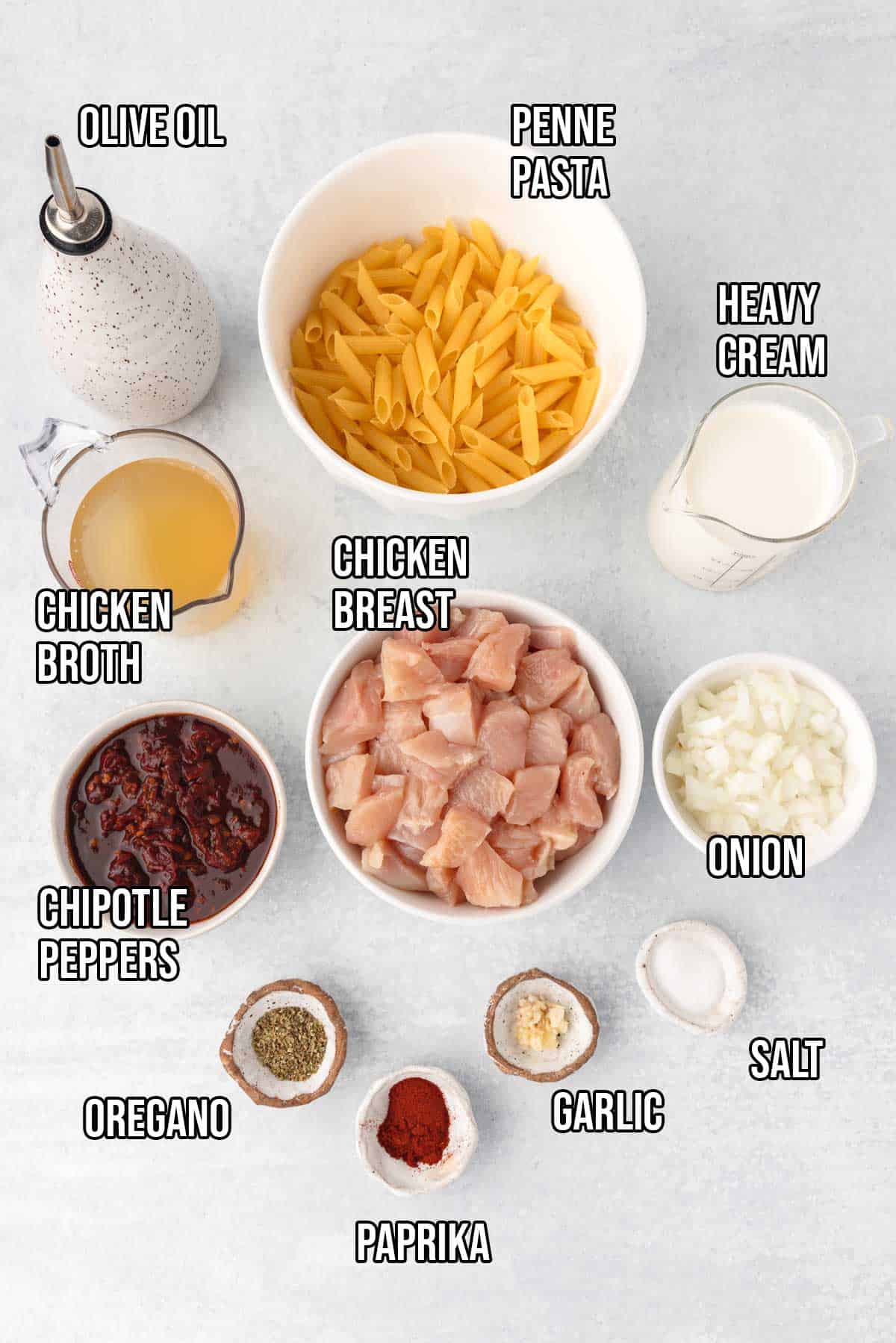 Spicy chipotle chicken pasta ingredients: chicken breasts cut into bite sized pieces, penne pasta, olive oil, minced garlic, diced onion, chipotle peppers in adobo sauce, chicken broth, heavy cream, paprika, dried oregano, and kosher salt.