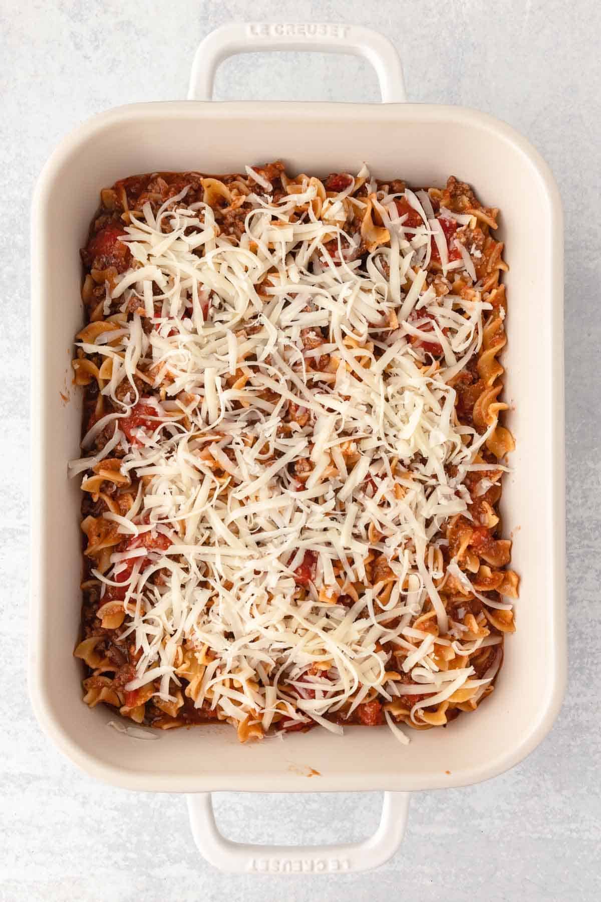 Beef and noodle mixture is spread into a prepared casserole dish and topped with an even layer of mozzarella shreds.
