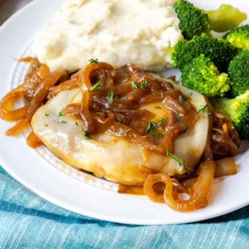 A pork chop topped with provolone and onions on a plate with mashed potatoes and broccoli.