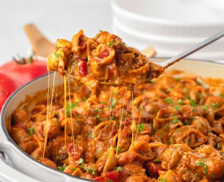 Shell pasta in a cheesy tomatoey sauce being scooped up into a serving spoon out of a large pot of pasta.