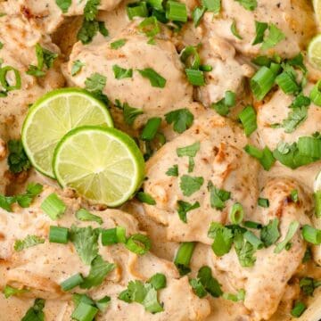 Close-up of chicken thighs in creamy sauce topped with green onions, cilantro, and lime slices.