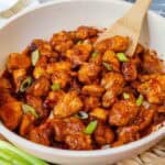 Close-up of honey-gochujang glazed chicken pieces topped with sliced green onions.