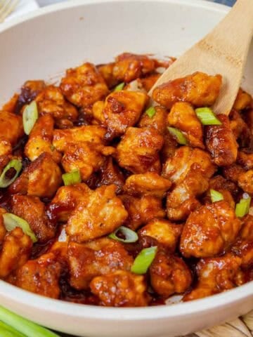Close-up of honey-gochujang glazed chicken pieces topped with sliced green onions.