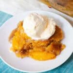 A plate of peach cobbler with vanilla ice cream on top.