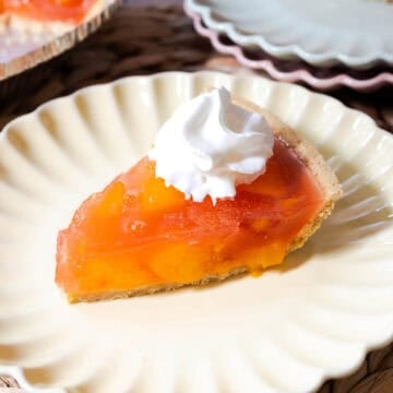 Peach jello pie with peach chunks set in peach gelatin in a graham cracker pie crust topped with whipped topping.