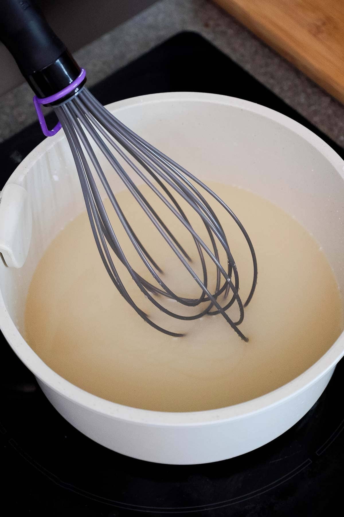 A saucepan with a whisk stirring water, sugar, and cornstarch.
