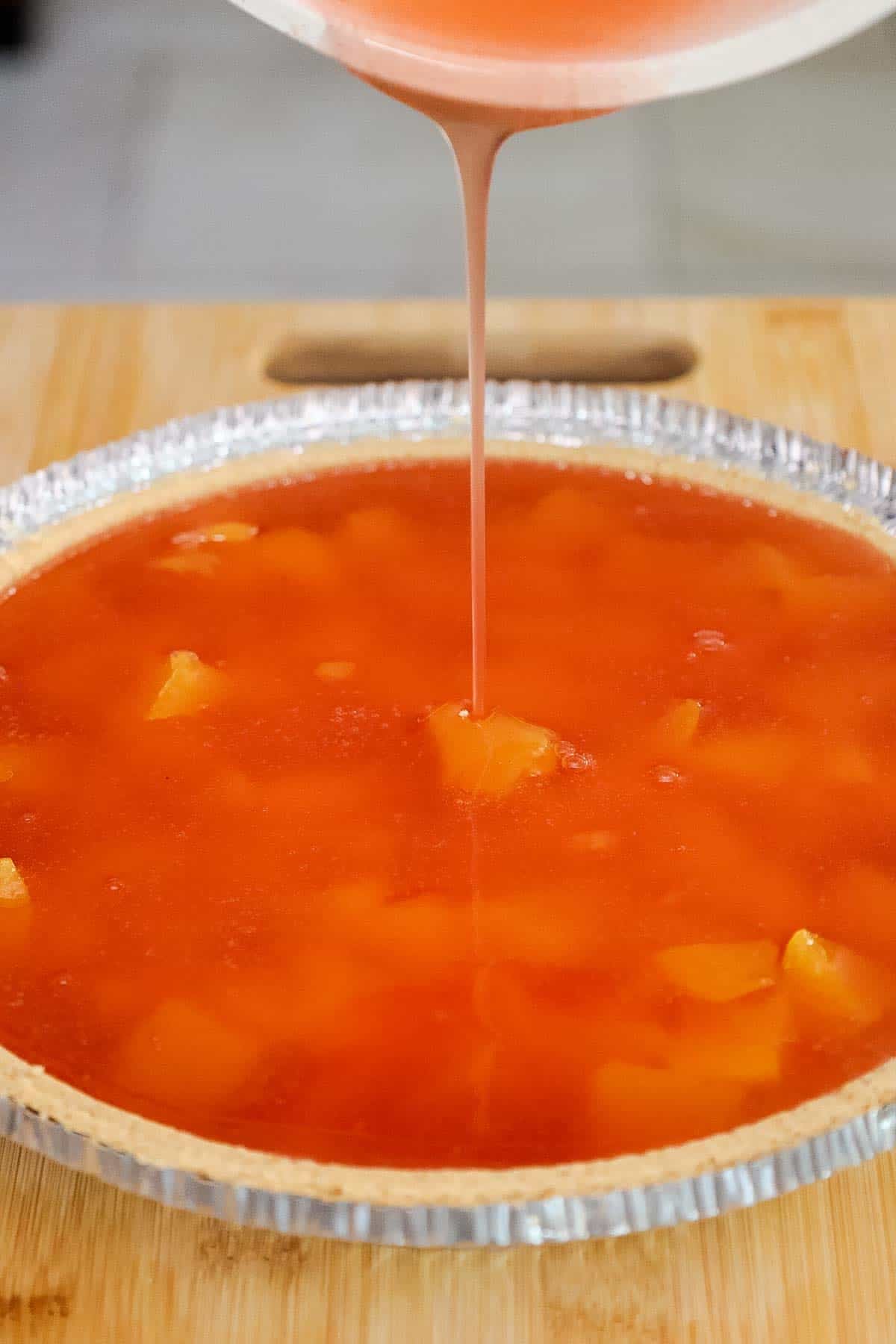 Peach gelatin mixture being poured over peaches in a pie crust.